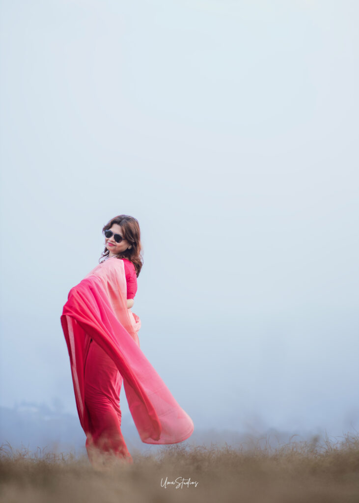 Elegant solo photoshoot in Munnar featuring a woman in a flowing pink saree against a misty hill backdrop, captured by Uma Studios Munnar